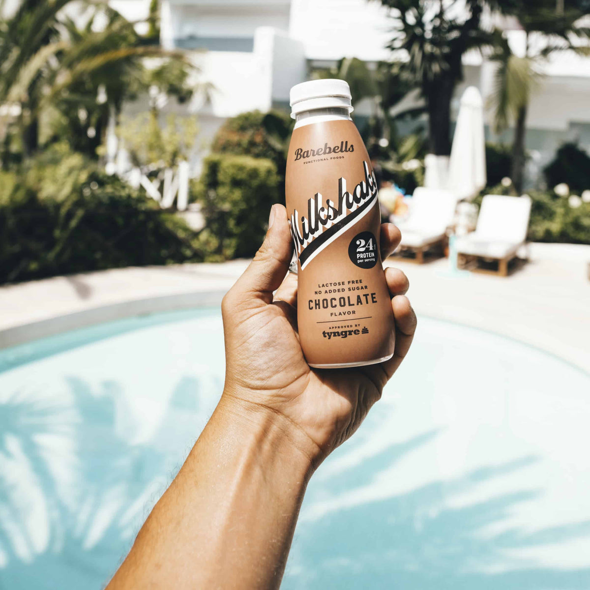 Barebells Milkshake Chocolate eiwitshake in de hand bij het zwembad - sfeerfoto